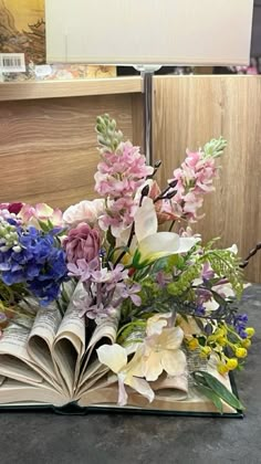 an open book sitting on top of a table filled with lots of different types of flowers