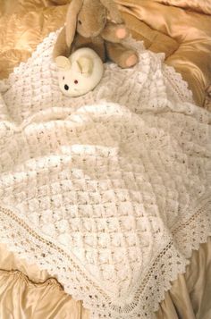 a teddy bear sitting on top of a bed next to a white crocheted blanket