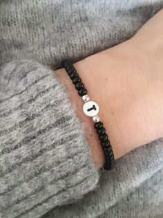 a person wearing a bracelet with a black cord and a white circle on the clasp