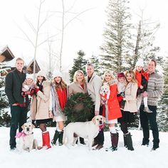 a group of people standing next to each other in the snow with two dogs and one cat