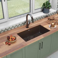 a kitchen sink sitting under a window next to a counter top with fruit on it