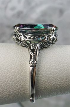 Natural Rainbow Mystic Topaz White Gold Ring Edward Design#70 Custom Here we have an Edwardian reproduction ring in 10K or 14K white gold filigree with a stunning Natural Rainbow Mystic Topaz gemstone solitaire. This full cut oval Topaz is 14mm in length and 10mm in width. This ring also sits 7mm off the finger. The inside of the band is marked 10K or 14K for gold, and can be engraved at request. Notice the beautiful leaf design of the gold filigree setting and etched band. This is a lovely rend Elegant Iridescent Topaz Gemstone Ring, Elegant Iridescent Topaz Ring For Anniversary, Iridescent Topaz Ring For Anniversary, Elegant Iridescent Rings For Formal Occasions, Elegant Iridescent Round Topaz Ring, Elegant Iridescent Rings With Accent Stones, Formal Iridescent Rings With Accent Stones, Iridescent Rings With Accent Stones For Formal Occasions, Iridescent Rings With Accent Stones For Formal Events