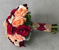 a bridal bouquet with red, pink and orange flowers on the floor in front of a gray background