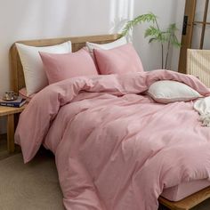 a bed with pink comforter and pillows in a room next to a plant on a table