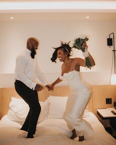 a man and woman are dancing on the bed in their hotel room, holding hands