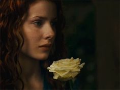 a woman with red hair holding a yellow rose