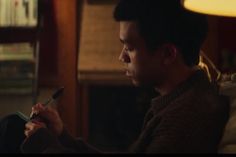 a young man sitting on a couch looking at his cell phone while holding a remote control