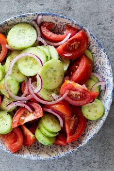 a blue and white bowl filled with cucumbers, onions, tomatoes and onion