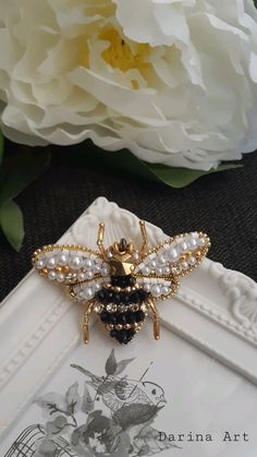 a bee brooch sitting on top of a white frame next to a bouquet of flowers