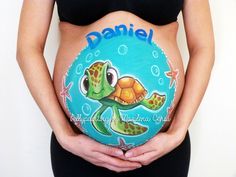 a pregnant woman holding a sea turtle painted on her belly with the name danielle written on it