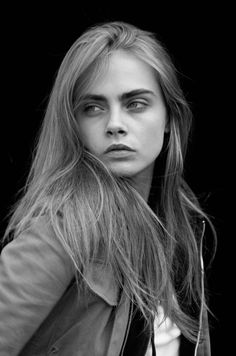 a black and white photo of a woman with long hair wearing a leather jacket looking at the camera