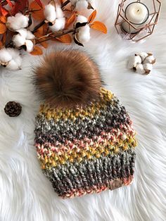 a knitted hat with a pom - pom sits on a fur rug next to cotton flowers