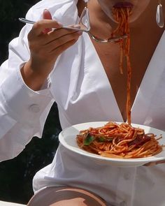 a woman is eating spaghetti from a white plate