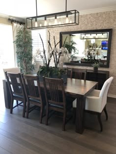 a dining room table with white chairs and a mirror on the wall in front of it