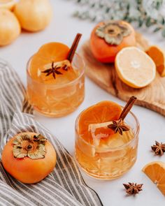 two glasses filled with oranges and cinnamon on top of a wooden cutting board next to sliced oranges