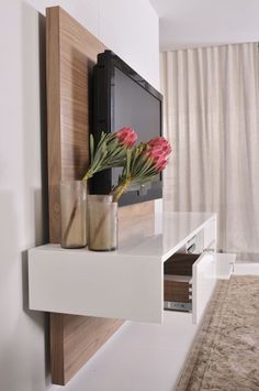 a vase with flowers sitting on top of a white shelf in front of a flat screen tv