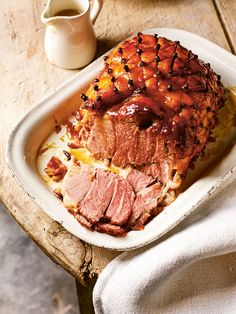 a roast beef covered in gravy on a white platter next to a cup of coffee