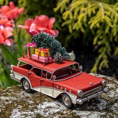 an old red car with presents on the roof is parked in front of some flowers