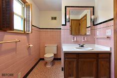 a bathroom with pink tile and wooden cabinets, mirror, toilet and sink in it