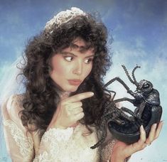 a woman in a white dress holding a black bug and pointing to it's side