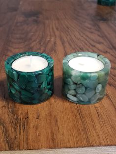 two candles sitting on top of a wooden table next to each other with rocks in them