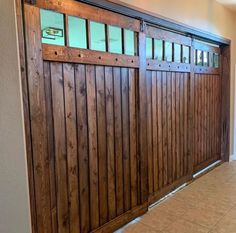 a wooden garage door with windows and bars on the top half, in front of a tiled floor