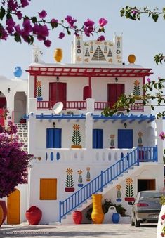 a white and blue building with flowers on the outside, stairs leading up to it