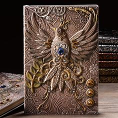 an intricately decorated book with blue eyes and feathers on the cover, sitting next to some books