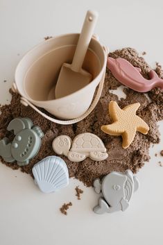 cookie cutters, sand and seashells on a white surface with an empty bowl