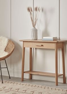 a wooden table sitting next to a white wall with a vase on top of it