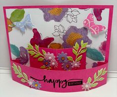 a pink birthday card with flowers and butterflies on the front, sitting on a white surface