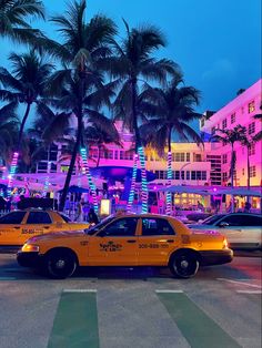 two taxi cabs are parked in front of palm trees and brightly lit buildings at night