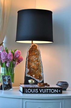 a table with a lamp and some flowers on it next to a book that says louis vuitton