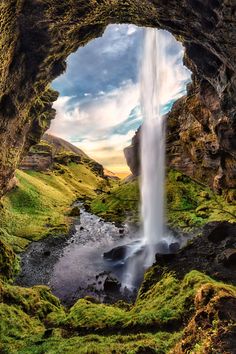 an image of a waterfall coming out of a cave into the ground with green grass