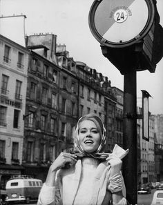 a woman standing next to a pole with a clock on it's face and scarf around her neck