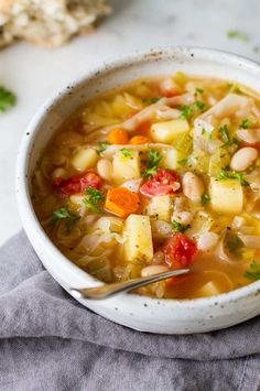 a white bowl filled with vegetable soup on top of a gray napkin next to bread