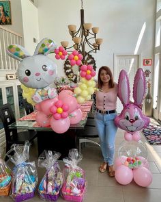 a woman standing in front of balloons and bunny ears on a table with other decorations