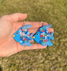 a hand holding two blue fish shaped earrings