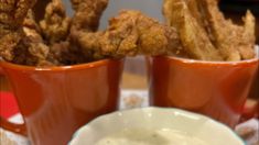 two cups filled with dipping sauce next to fried food