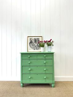 a green chest of drawers with flowers on top and a framed photo in the corner