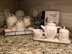 the tea set is sitting on the kitchen counter next to two mugs and a sign