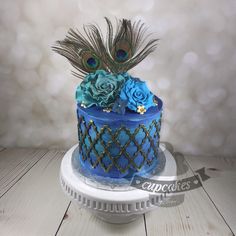 a blue cake decorated with flowers and peacock feathers