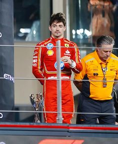 two men in red and yellow uniforms standing next to each other on a race track