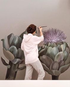 a woman is painting a large purple flower on the side of a wall with succulents