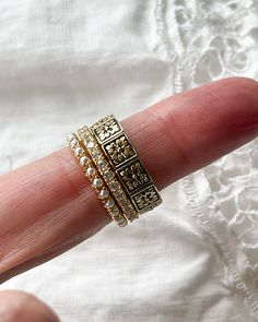 a woman's hand with three gold rings on top of her finger and the ring has four different designs