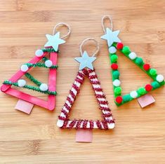 three christmas trees made out of popsicle sticks on a wooden surface with pom - poms