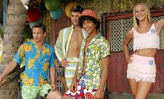 three men and two women standing in front of a hut with palm trees on the porch