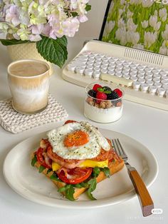 a plate topped with an egg sandwich next to a cup of coffee and a computer keyboard