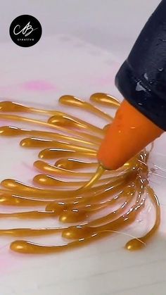 a person is painting gold swirls on a white surface with a black marker and orange ink