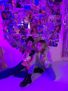 two people sitting on the floor in front of a wall covered with pictures and posters